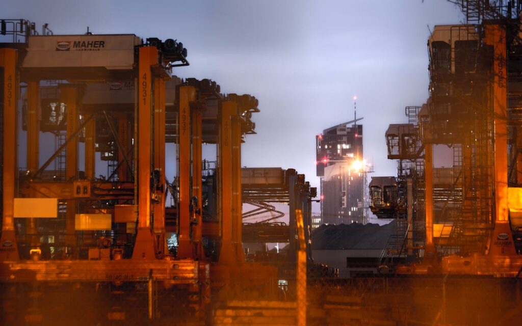 A view of cranes in Gdynia Harbour with city skyline at night, highlighting industrial activity.